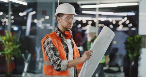 Portrait of Professional Construction Worker in Protective Vest and Helmet Looking Into Building