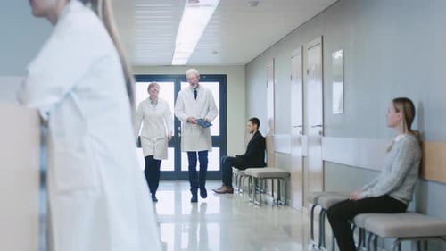 In the Hospital Two Doctors Walking Through the Hospital Hallway, They Talk and Share Tablet Comput