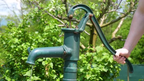 Hands of a White Man Pumps Water from a Well Closeup Shot in a Green Garden, Traditional Equipment,