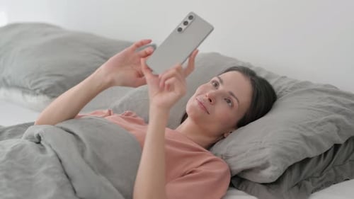 Young Woman Relaxes in Bed with Phone