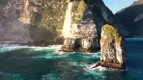 Aerial view of turquoise ocean waves crashing coastline of Nusa penida island, one of the tourist at