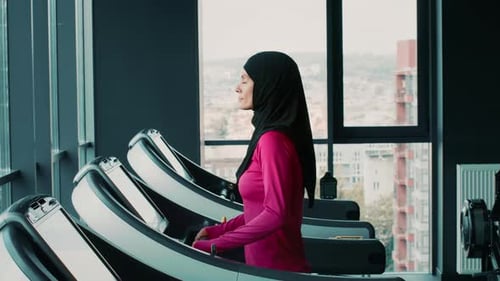 Woman With Light Skin in Pink Top Exercising on Treadmill in Gym With Large Windows
