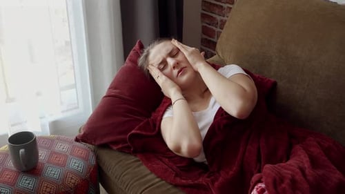 Jeune femme malade ayant de la fièvre allongée sur le canapé et se touchant le front