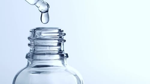 Drop Of Liquid Falling From Glass Lab Pipette In Transparent Bottle