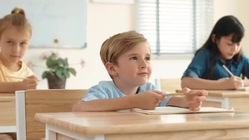 Children at Desks Writing and Listening in Classroom
