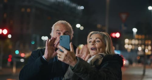 A happy senior couple is making a selfie or video call with a smartphone in a city center in the e