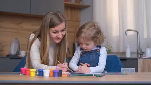 Woman and Child Drawing Together at Table Indoors