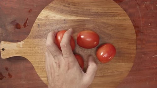 Hand Placing Fresh Tomatoes on a Wooden Cutting Board