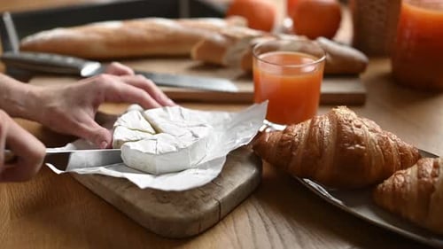 Person Cuts Cheese Next to Croissants and Orange Juice