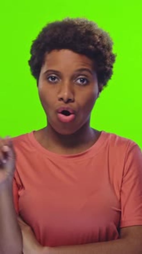 Woman with Orange Shirt Gestures Toward Camera in Front of Bright Green Screen