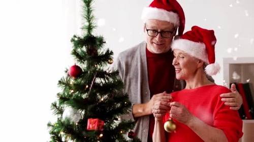 Elderly Couple Decorating Christmas Tree Wearing Santa Hats