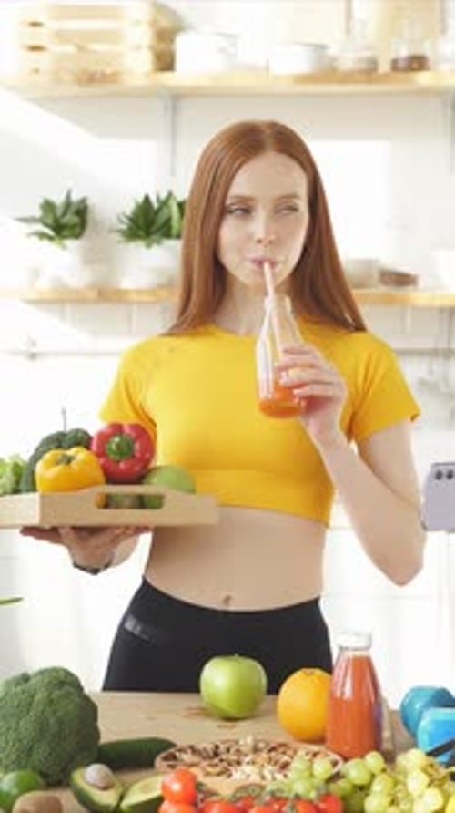 Red-Haired Woman Drinks Juice, Holds Tray of Vegetables