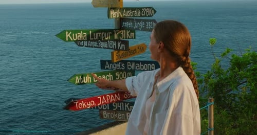 Woman traveler pointing a wooden directional post while looking out at the vast blue ocean horizon