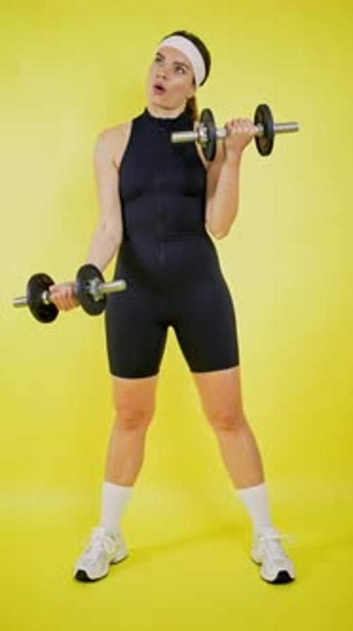 Woman in Fitness Outfit Lifting Weights on Yellow Background