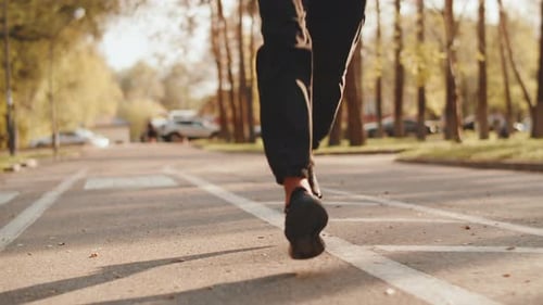 Legs of an Athlete in Sportswear Close Up Who Running Fast on the Path of a City Park on a Sunny Day