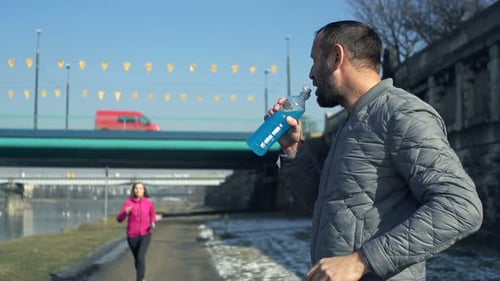 Male Jogger Drinking Isotonic Drink and Woman Running in City, Super Slow