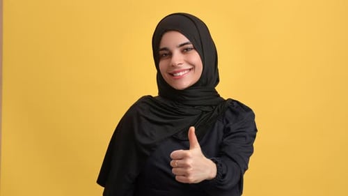 Portrait Smiling Turkish Woman in Black Hijab Showing Cool Thumb Up Gesture Posing Isolated Orange