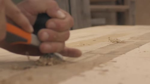 Low angle slow motion close up of a carpenter using a planer on wood boards in his shop