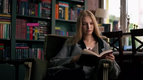 Woman Reading Book in Armchair by Bookshelf