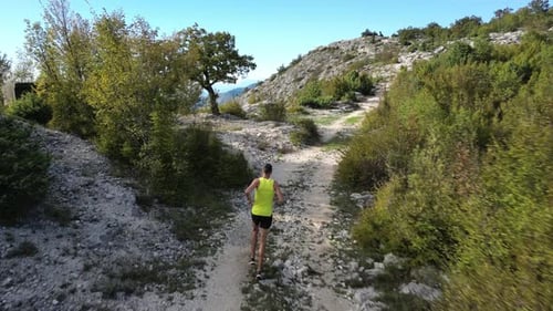 Runner Jogging in Shorts and Tshirt on Mountain Road with Trees and Beautiful Scenery in Background