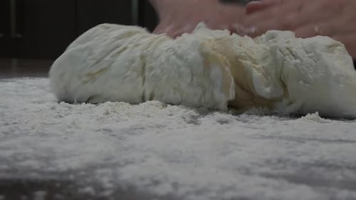 Pan around female hands preparing and kneeding freshly made sourdough bread on top of kitchen bench