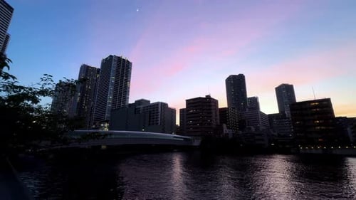 City skyline at dusk with colorful sunset reflecting on a calm river