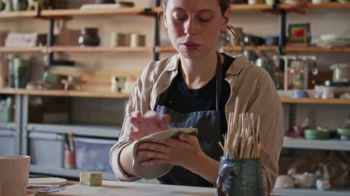 Female Artisan Smoothing Surface of Handmade Clay Plate in Pottery Studio
