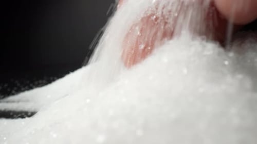 White sugar cascades from a hand against a captivating black backdrop