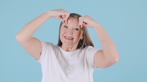Senior Woman Demonstrates Facial Exercises for Skin Care in a Bright Blue Studio During Daytime
