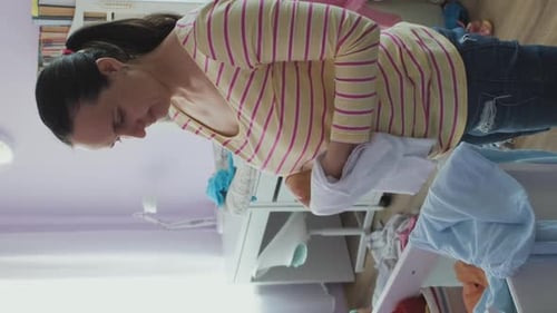 Woman Folds Baby Clothes in a Child's Room