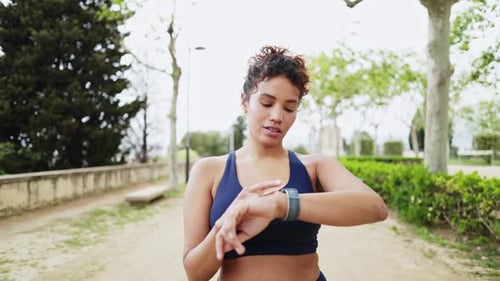 Jovem mulher esportiva verificando smartwatch em câmera lenta