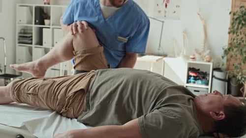 Physical Therapist Stretching Man's Leg in Bright Office