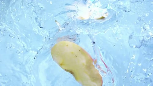 Fresh Apple Slices Falling into Swirling Blue Water