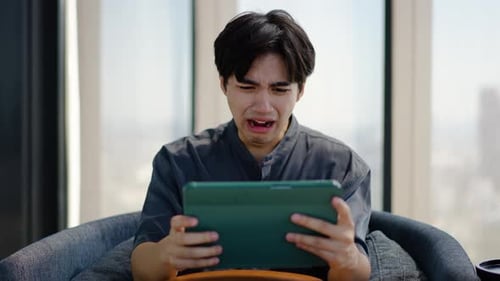 Distraught Young Adult Using Tablet in Armchair