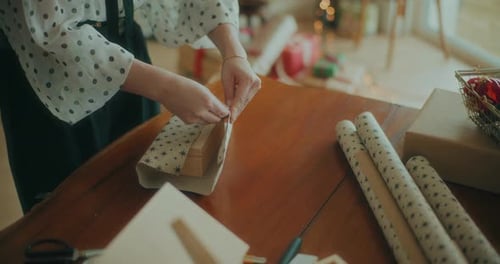 Hands Wrapping Gifts at a Wooden Table