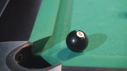 Black Billiard Ball Rolling Toward Pool Pocket After Cue Ball Strike