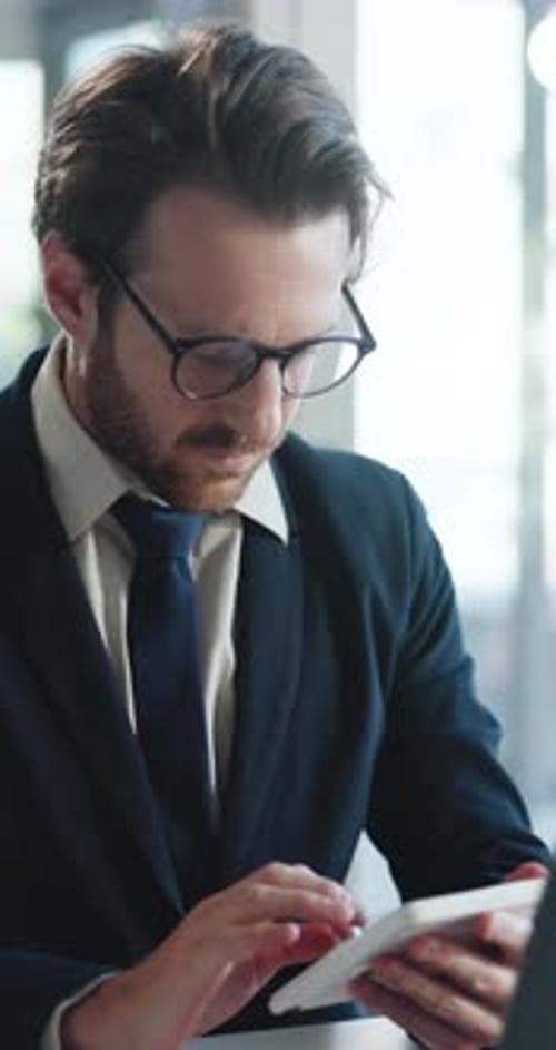 Serious Man Works on Tablet and Laptop at Desk