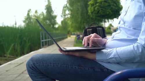 A man works with a laptop while sitting on a bench on the coast