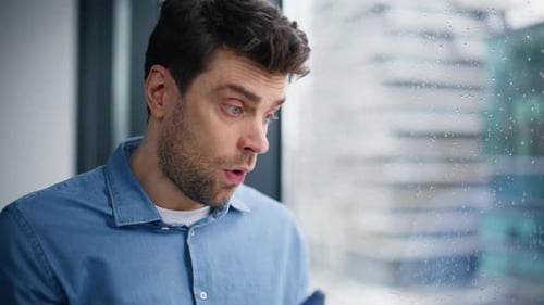 Thoughtful Man Gazing out Rainy Window After Phone Call