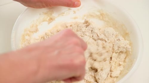 Close-up of a person using a spoon to mix flour and liquid in a bowl, preparing dough for home bakin