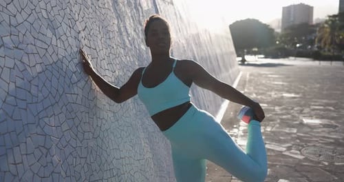 Athletic woman stretches quadriceps muscle against wall outdoors