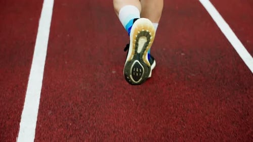 Closeup of the Legs of a Man Running Through the Stadium Rear View