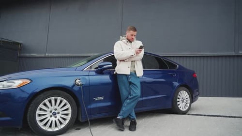Young Adult Charging Electric Car Using Phone