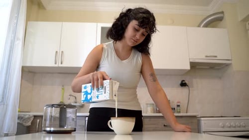 Young Adult Pouring Milk into Cup in Kitchen