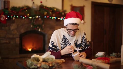 Young Adult Opening Christmas Gift by Fireplace