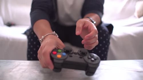 Woman's hands using gamepad close-up view playing video console game at home sitting on the sofa.