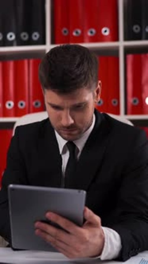Vertical of Businessman Writing Notes From Ipad in Business Office