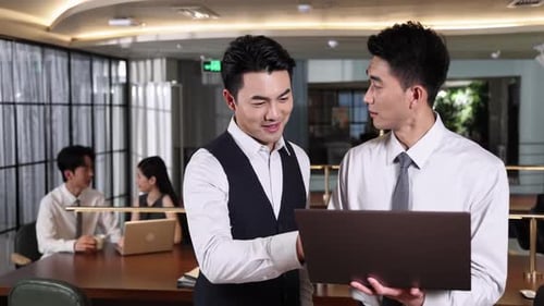 Two smiling male colleagues in office setting discussing business project on laptop. Financial advis