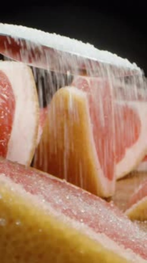 Vertical video. I sprinkle a spoonful of sugar onto the slices of bitter grapefruit with red flesh.