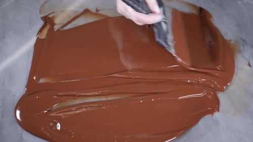 Tempering Chocolate Chef Mixes Melted Chocolate with Metal Spatula on Stone Table in Pastry Shop